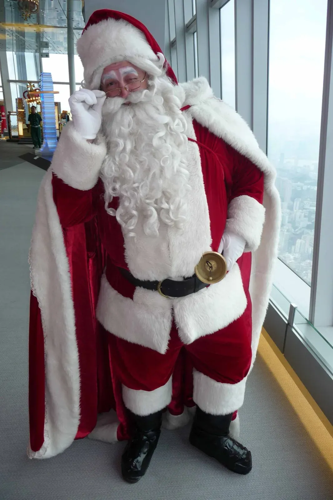 Western Santa with a hand bell posing by the windows of a high-rise in Hong Kong