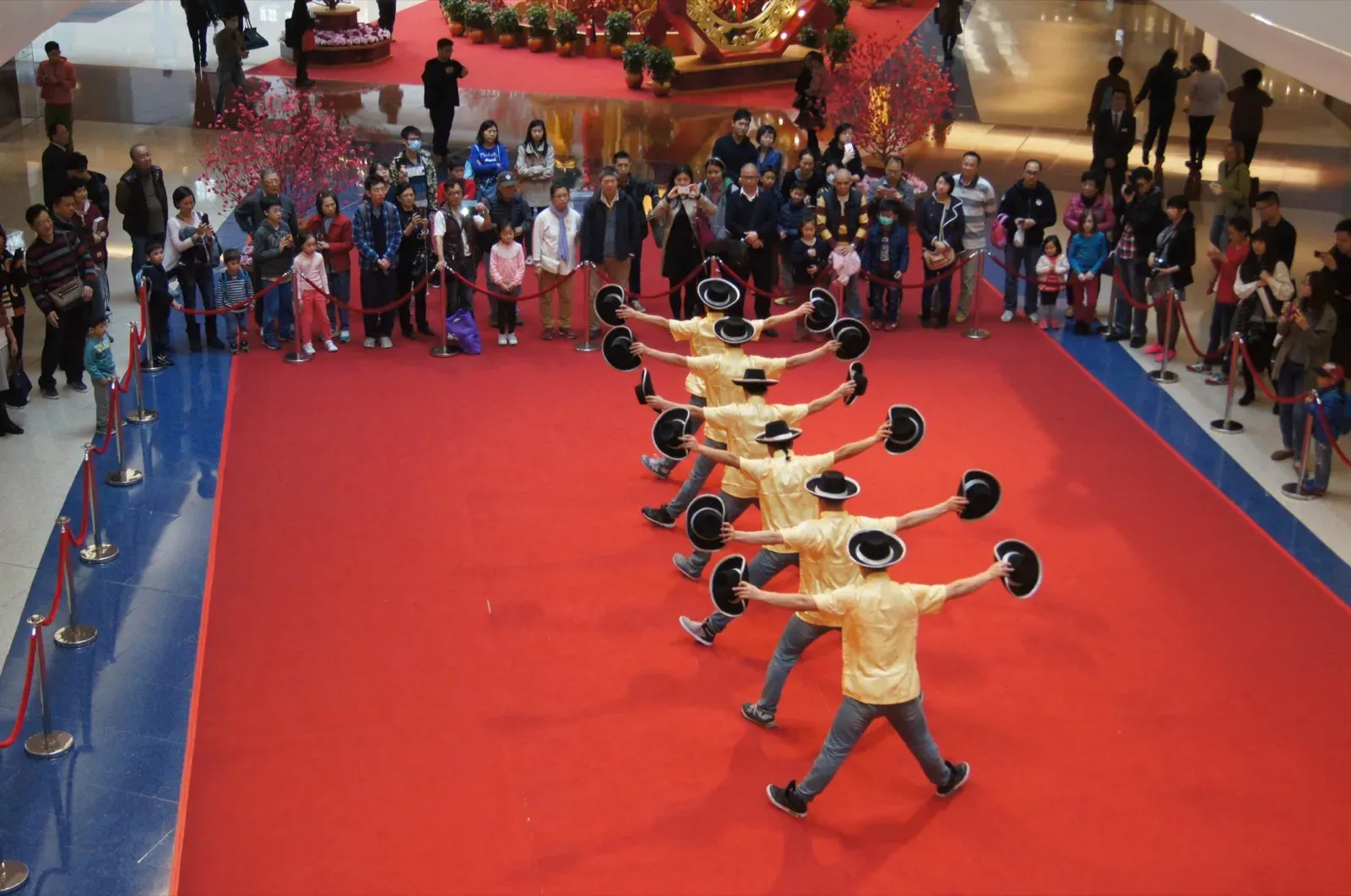 Line of performers in yellow shirts and black hats doing a synchronised hat routine for Chinese New Year at Festival Walk, Hong Kong