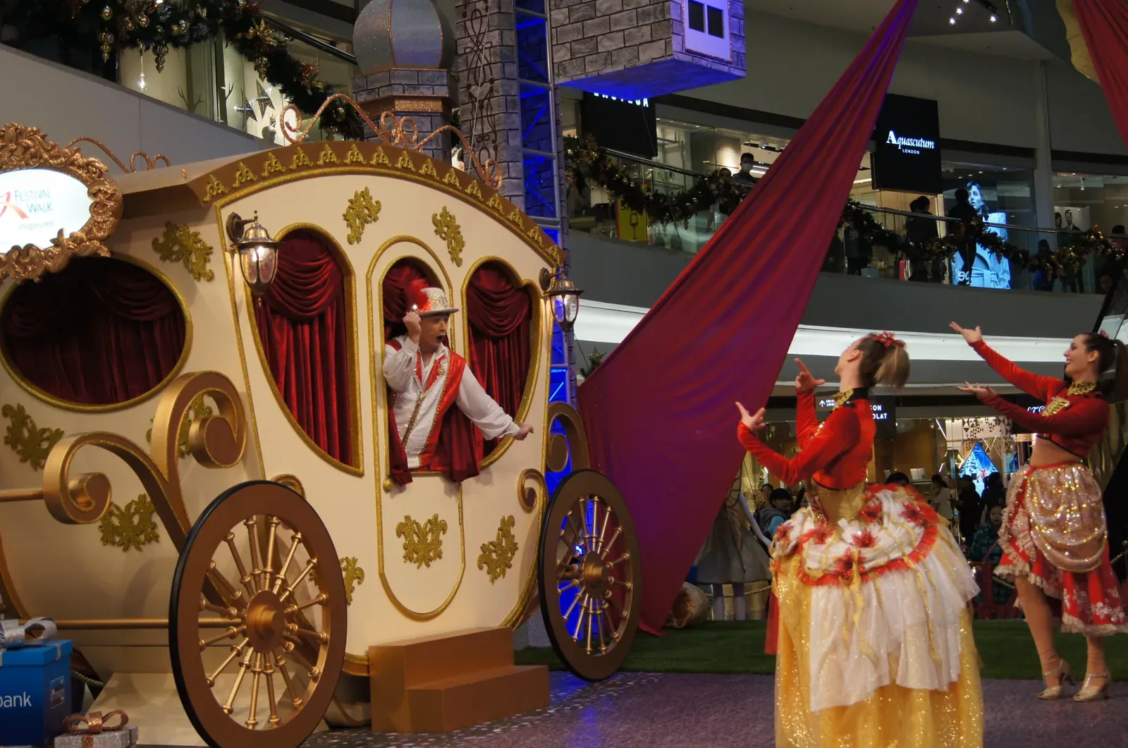 Christmas show at Festival Walk: a performer waves from a golden carriage beside two dancers in red and gold costumes