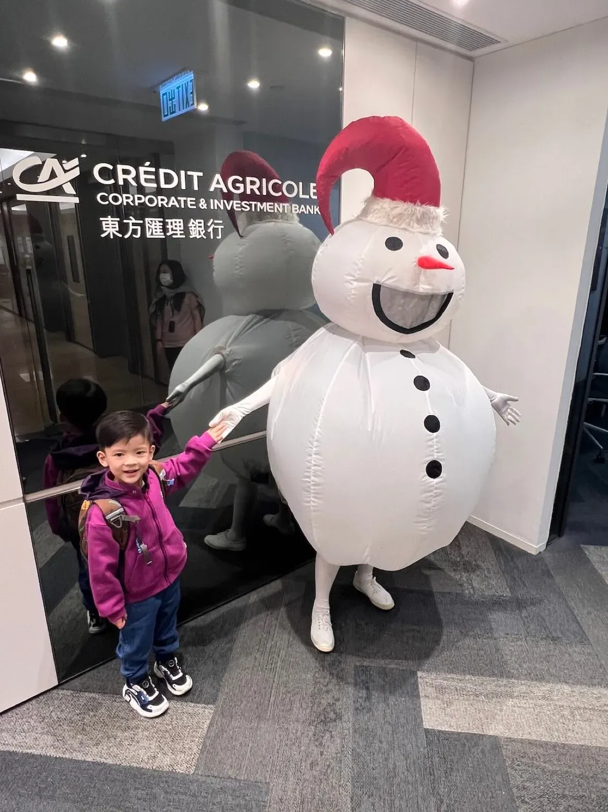 Inflatable snowman mascot in a Santa hat with a child outside a Crédit Agricole office in Hong Kong