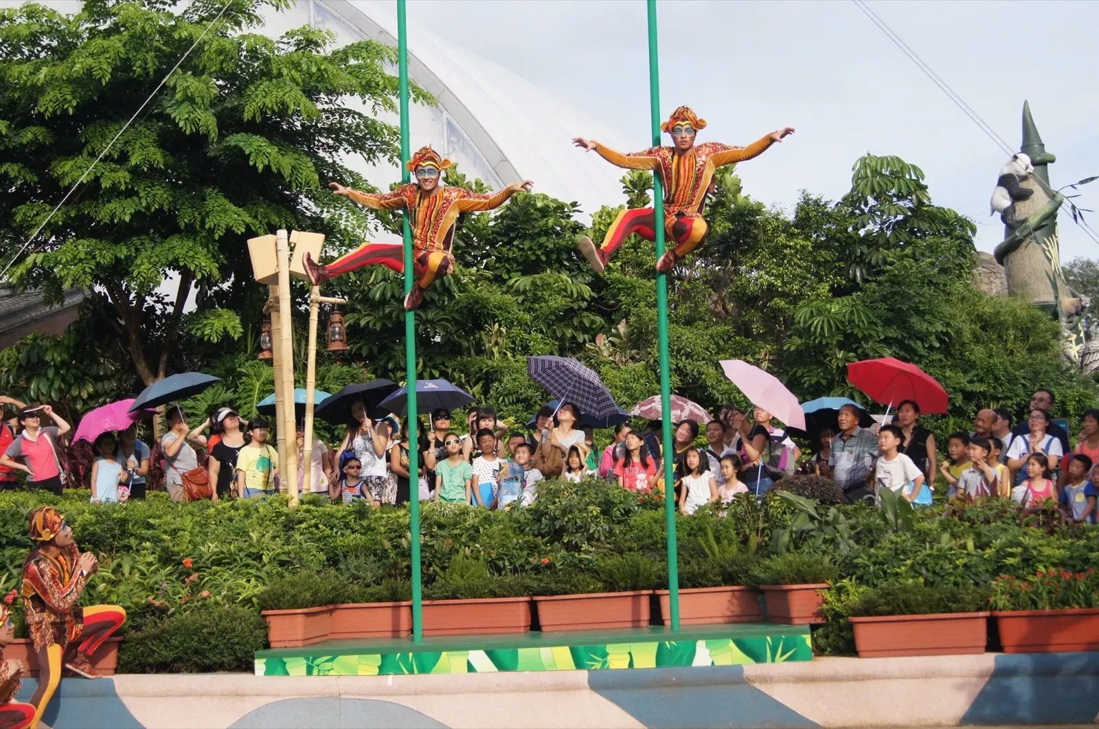 Pole acrobats performing above a crowd with umbrellas at Ocean Park in Hong Kong
