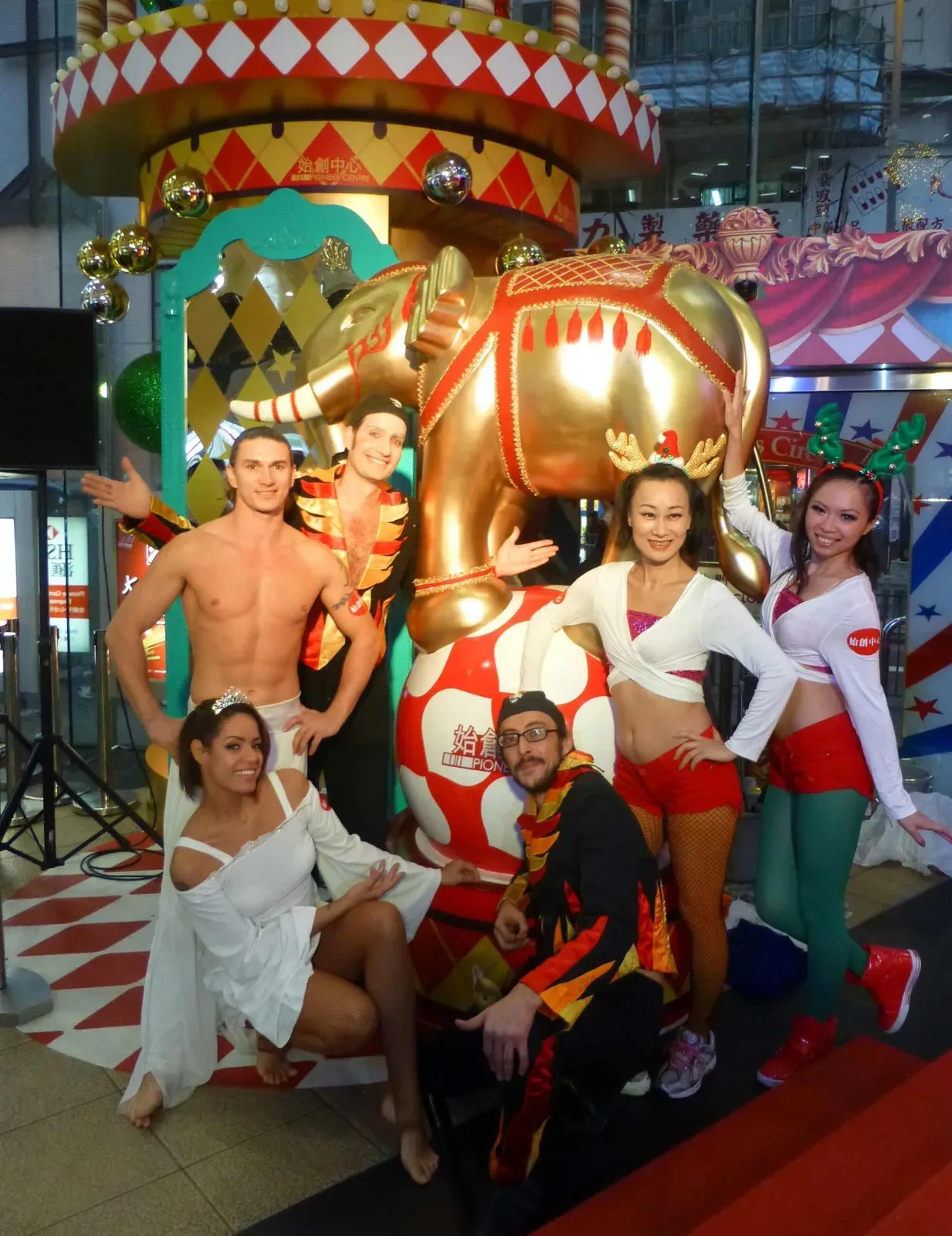 Circus team in white and red posing on a colourful stage in a shopping mall