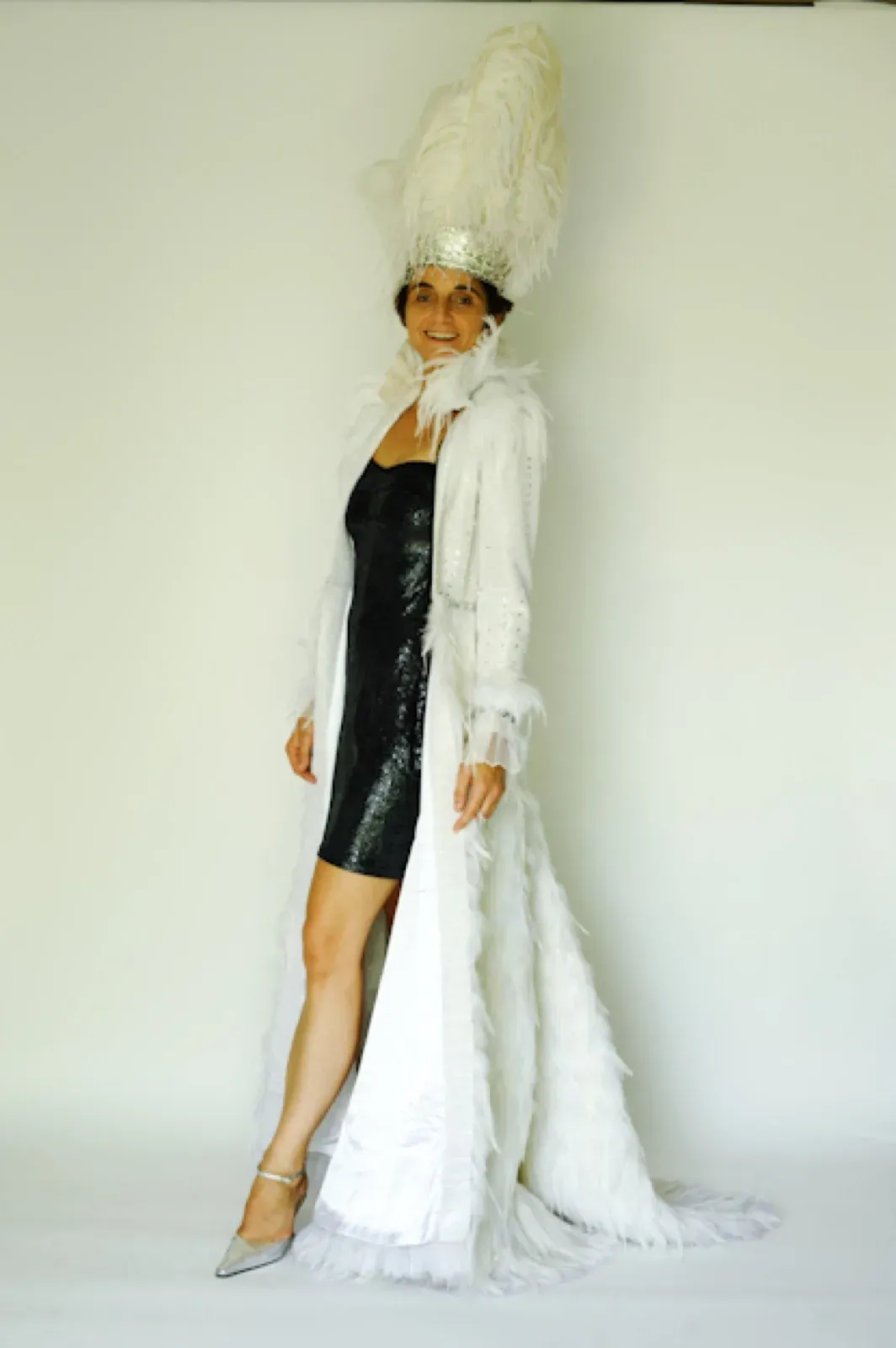 Female performer in a white feather headdress, white feather coat and black sequin dress