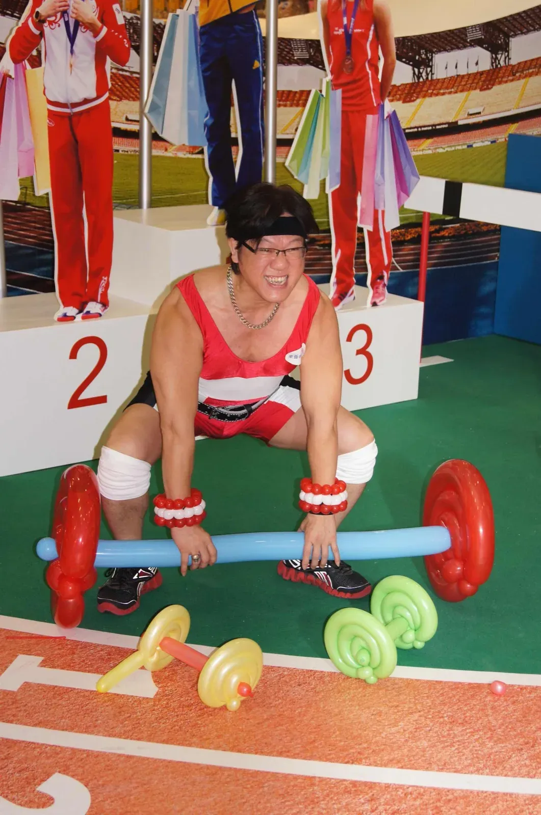 Balloon twister dressed as a weightlifter lifting a balloon barbell on a podium