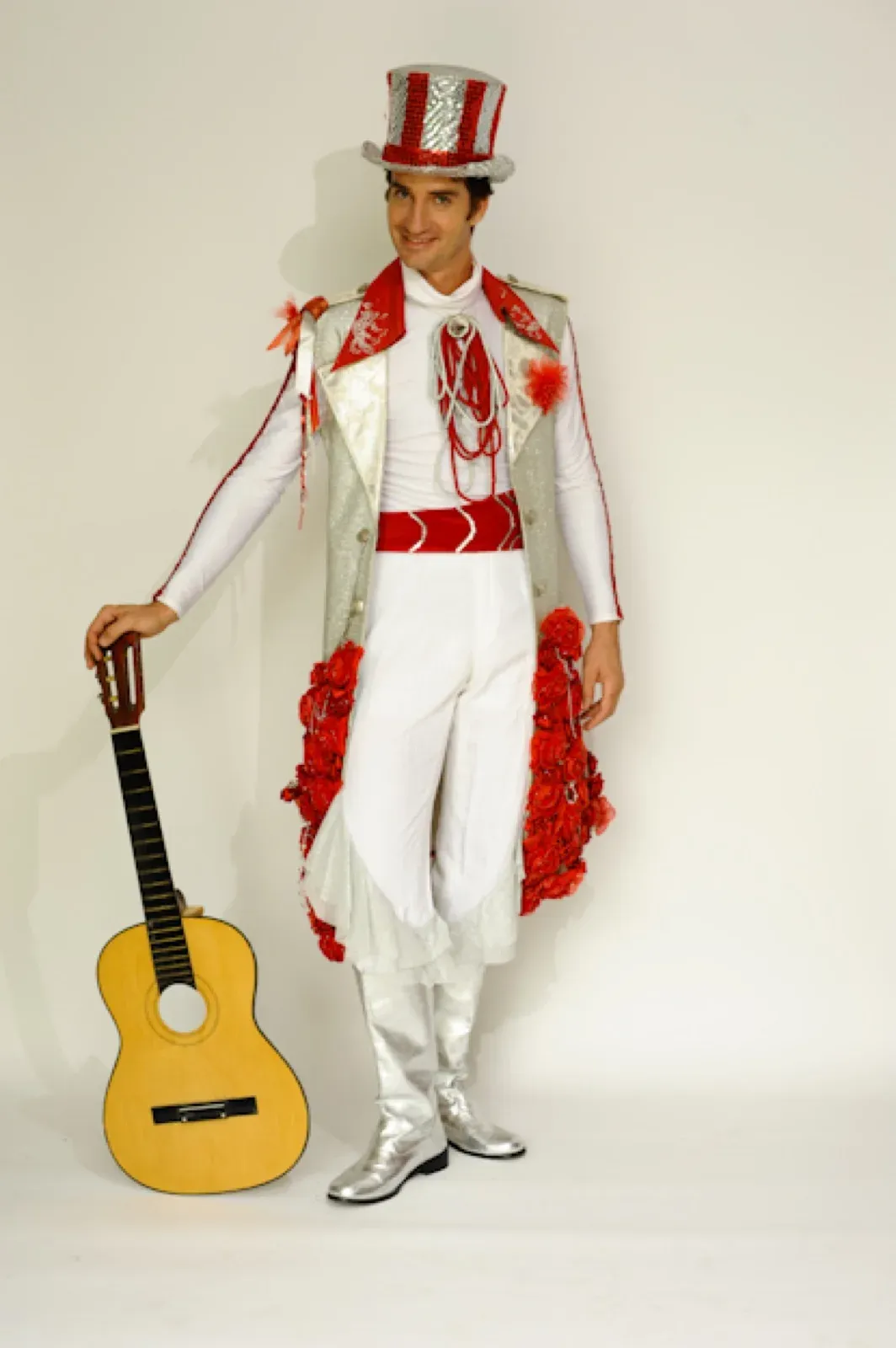 Musician in a white, silver and red costume with a top hat, holding a guitar