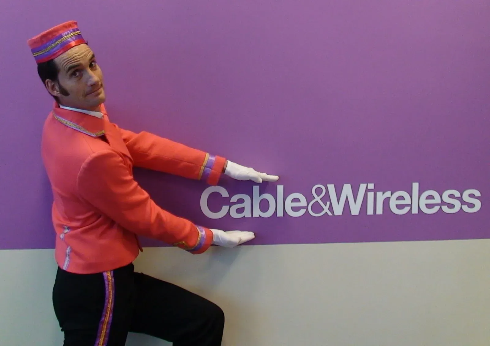 Performer in a pink bellboy uniform beside a Cable & Wireless sign