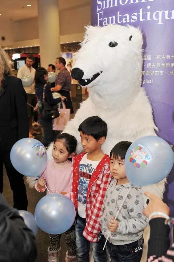 Tall polar bear mascot posing with children holding balloons