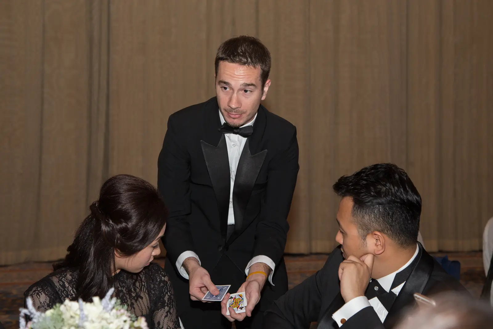 Magician on stage at the Asia Boating Awards producing cards, with two assistants in black