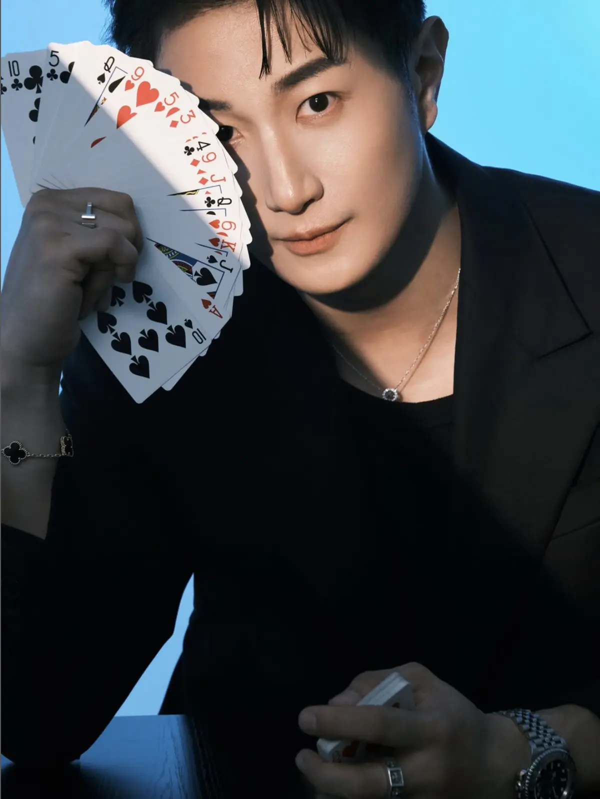 Magician in black holding a fan of playing cards beside his face against a blue background