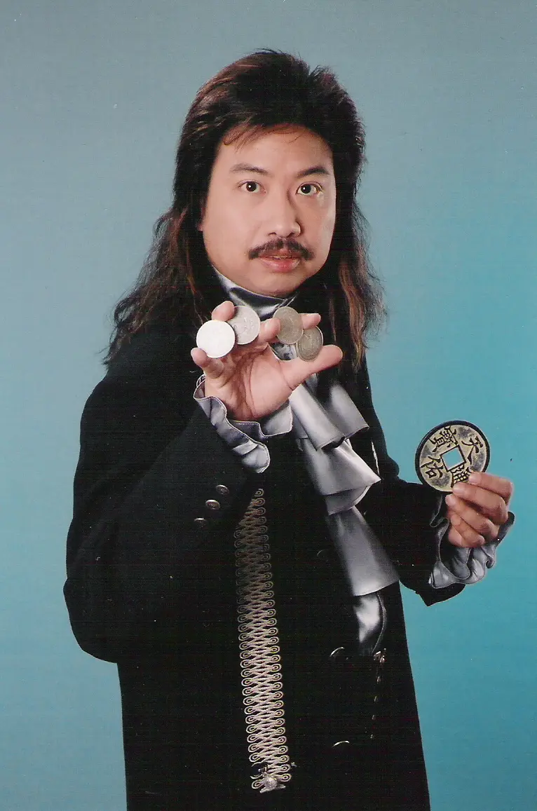 Close-up magician in a black suit holding a fan of cards beside a guest