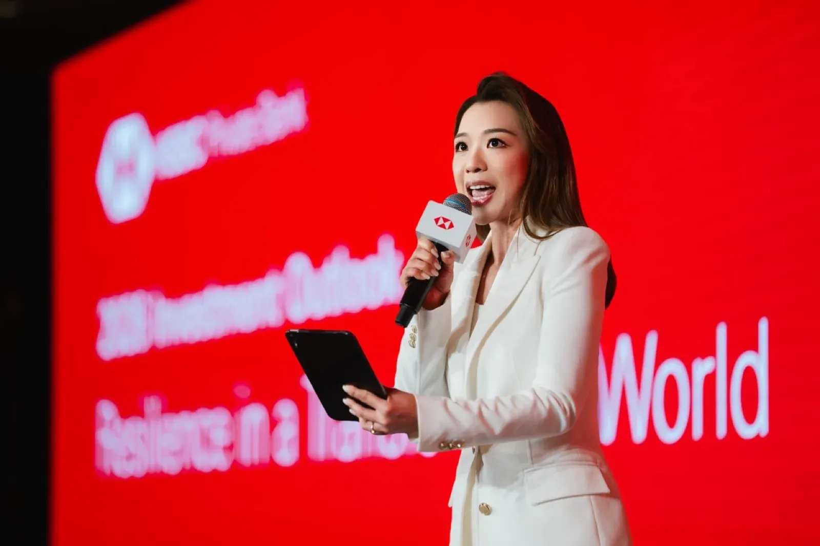 Emcee in a white suit hosting a corporate event on stage in front of a red screen