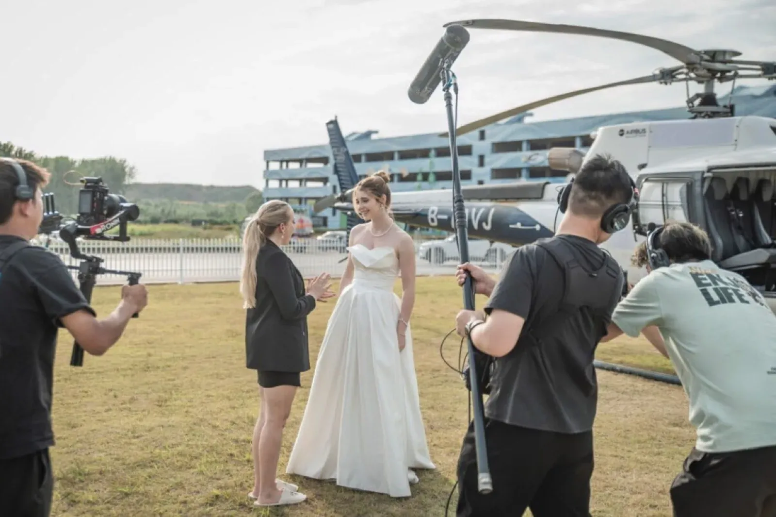 Behind-the-scenes movie shoot with an actress in a white gown beside a helicopter in Hong Kong