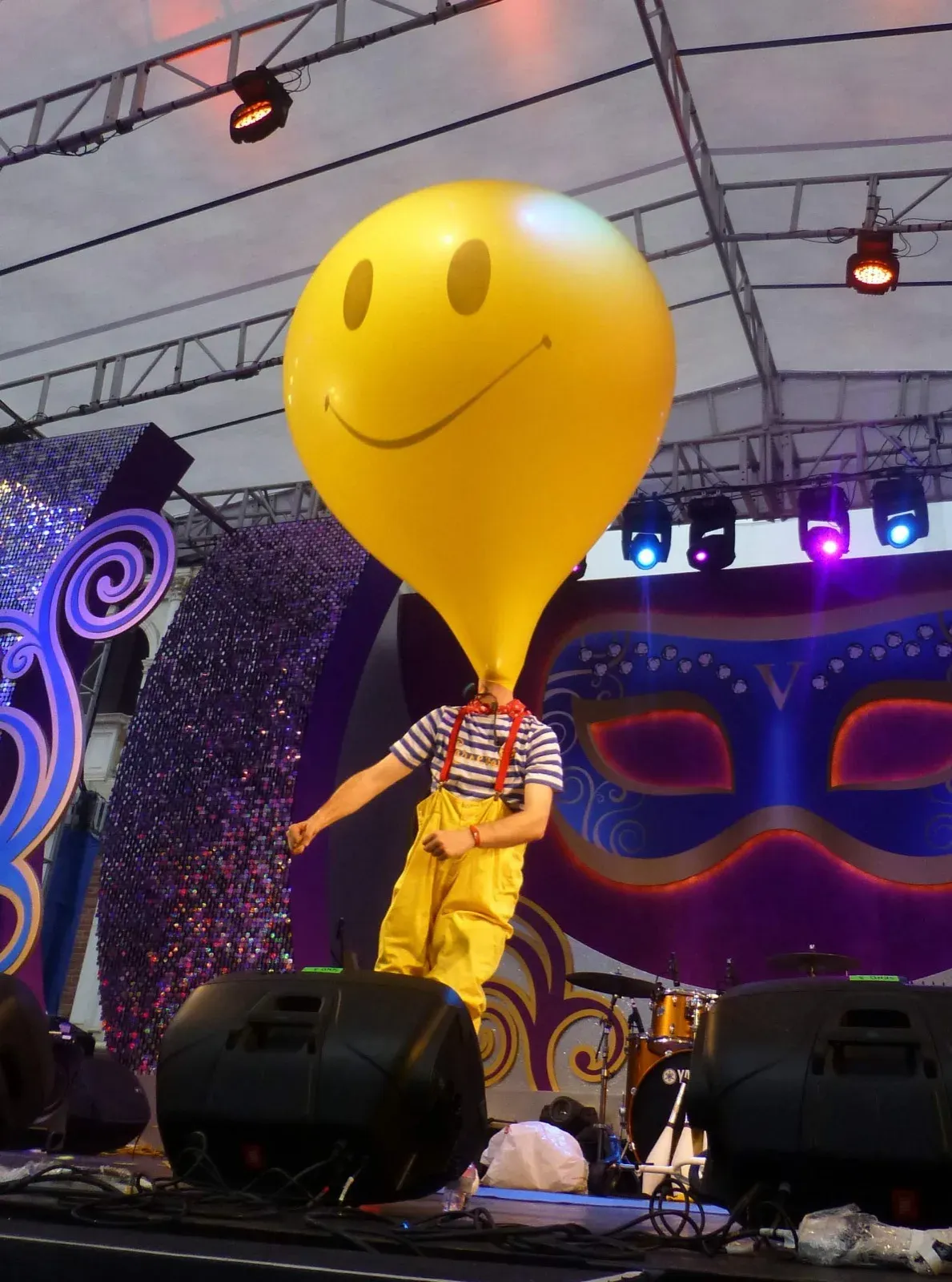Performer with a giant smiley balloon head on a carnival-themed stage