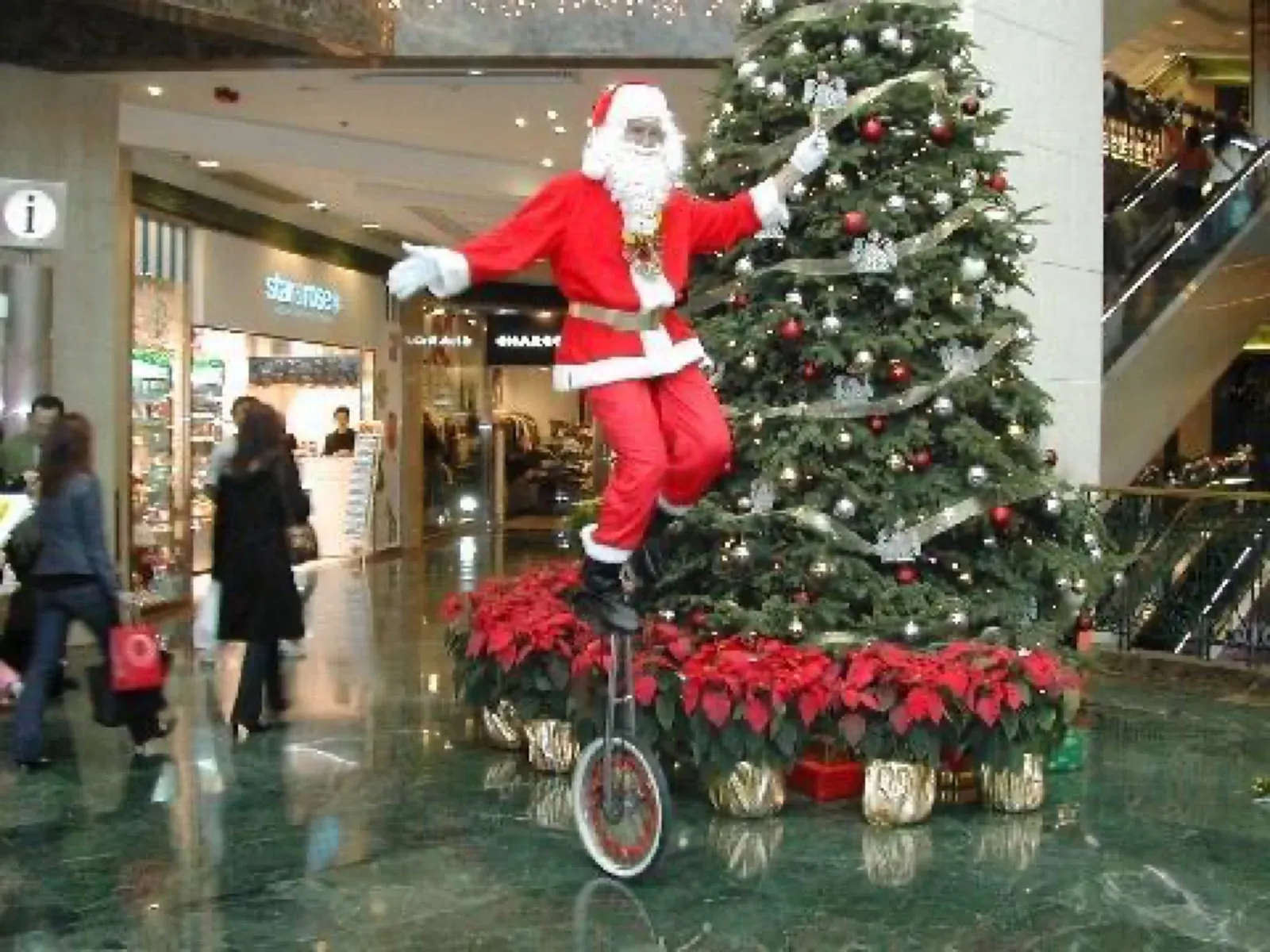 Santa Claus riding a tall unicycle beside a Christmas tree in a Hong Kong shopping mall