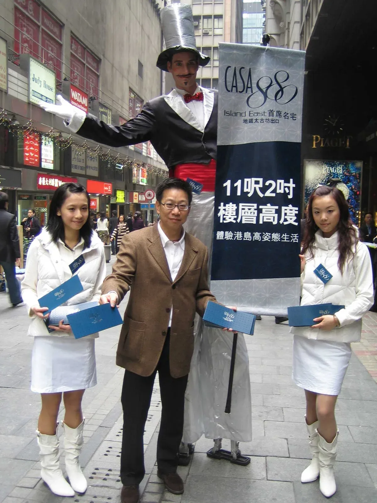 Stilts walker holding a new property launch banner with promoters on a Hong Kong street