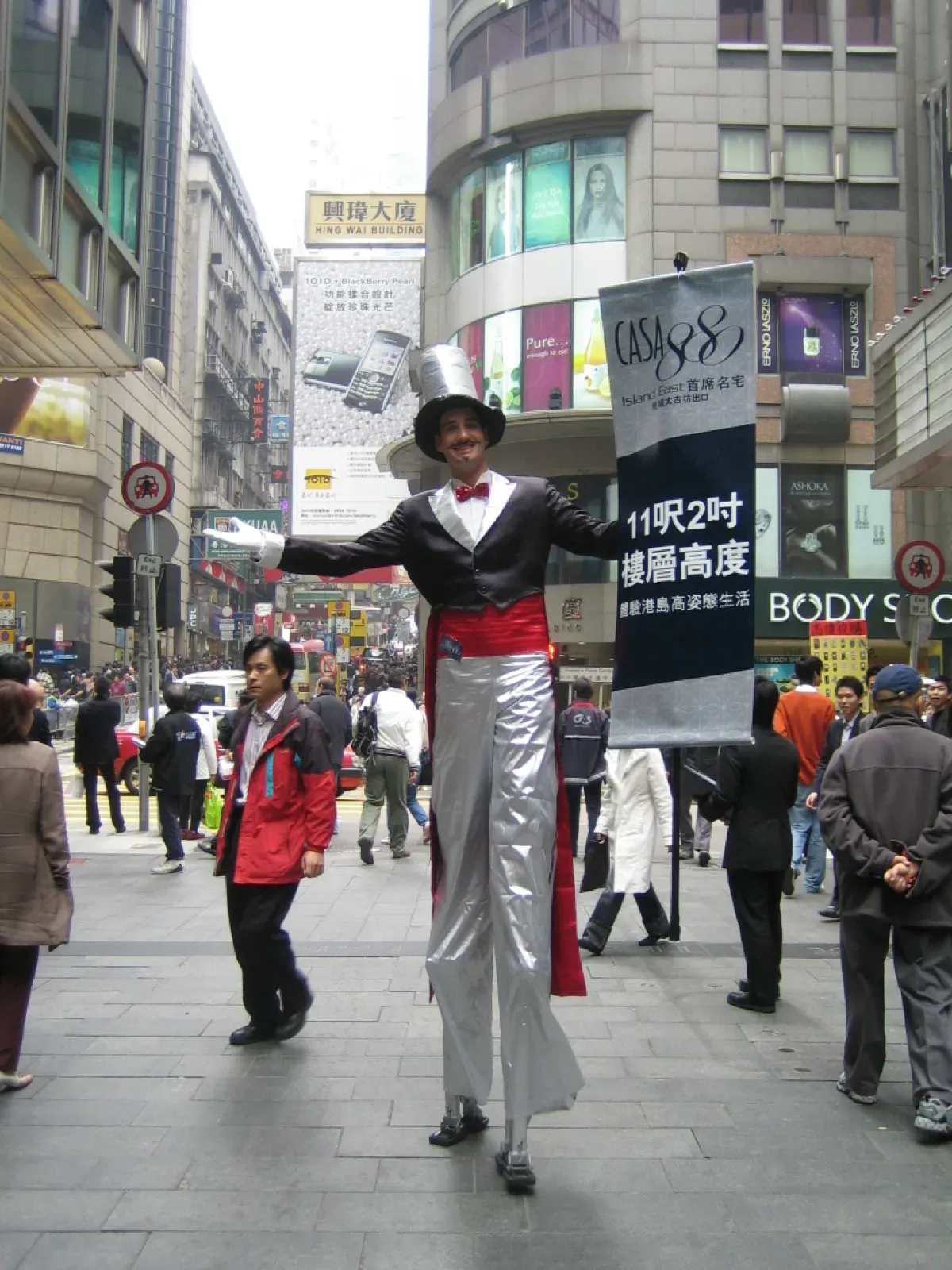 Tall stilts walker in a top hat and white trousers on a busy Hong Kong street for a property promotion