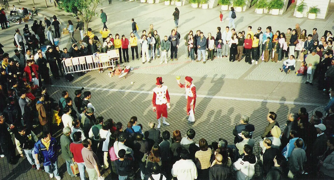 Two performers in red and white costumes in the middle of a large circle of spectators at an outdoor street show