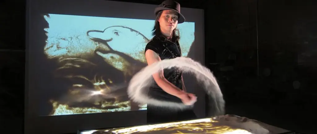 Sand artist drawing a dolphin on a light table during a visual act in Hong Kong